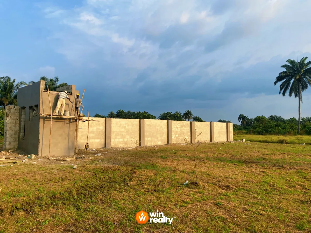 Amazon Estate, behind Wigwe University in Isiokpo: perimeter wall under construction, with workers and surrounding palm trees.