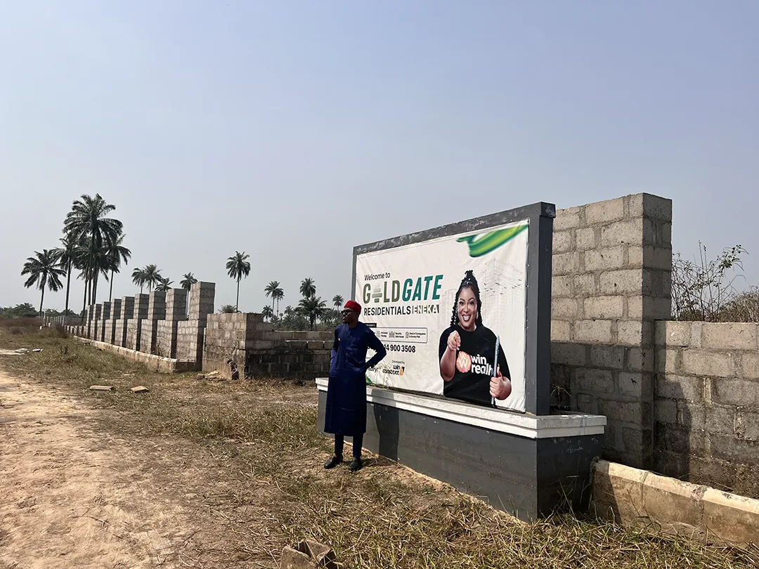 Goldgate Residentials in Eneka: sign beside its boundary wall, with a Win Realty representative and palm trees.
